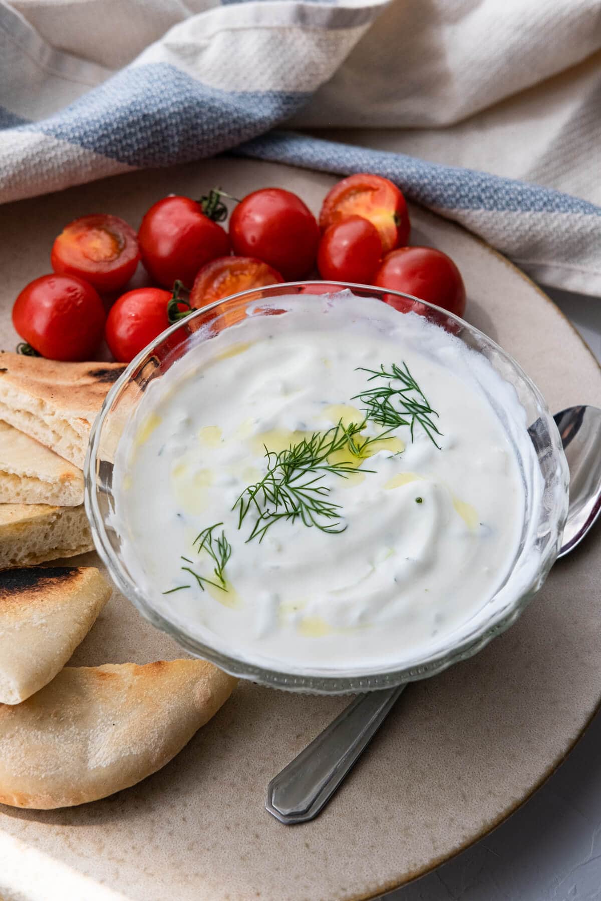 Rich and creamy classic tzatziki sauce served in a small bowl alongside cherry tomatoes and pita bread. 