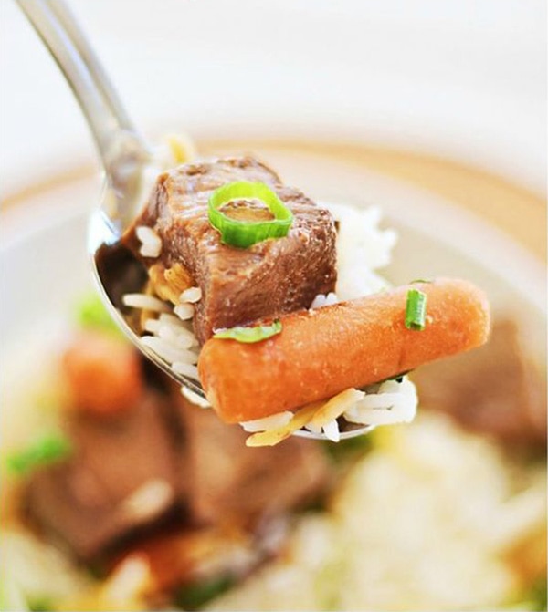 Asian stewed beef and baby carrots on a spoon.