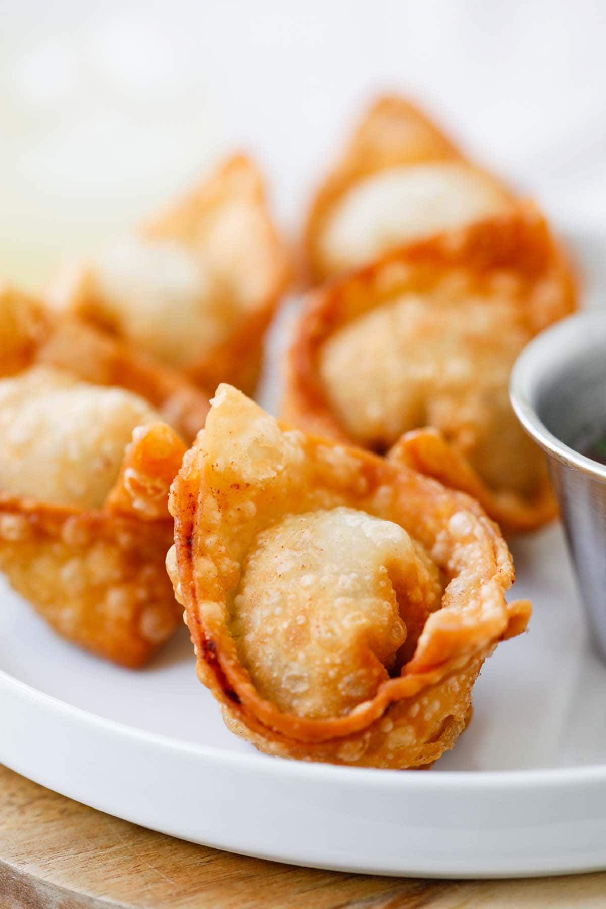 Perfectly brown fried wontons on serving dish with side of sweet and sour sauce.
