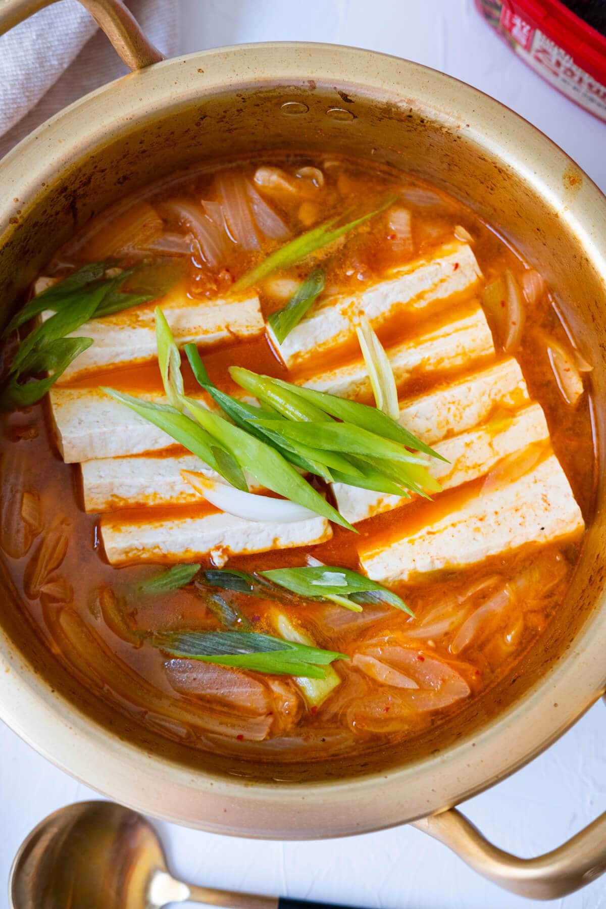 Easy kimchi jjigae in a soup pot with a spoon and gojuchang on the side. 