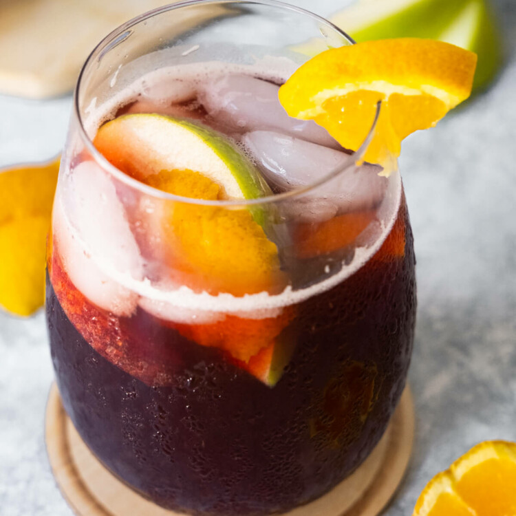 Spanish sangria in a glass with apple and orange slices aside.
