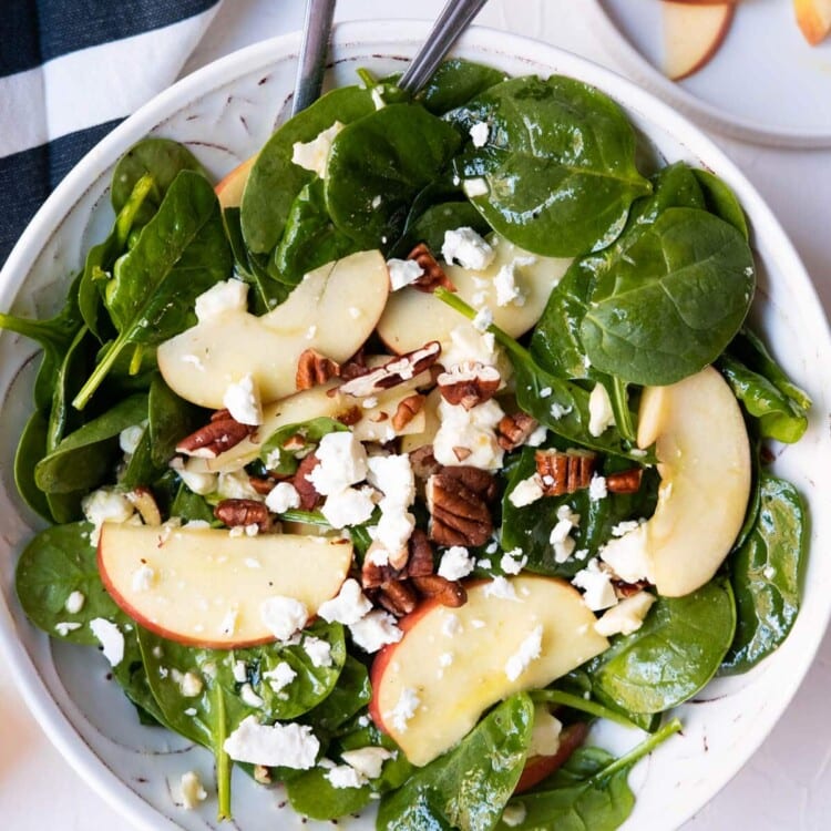 Spinach salad with apples, walnuts and feta cheese on top.